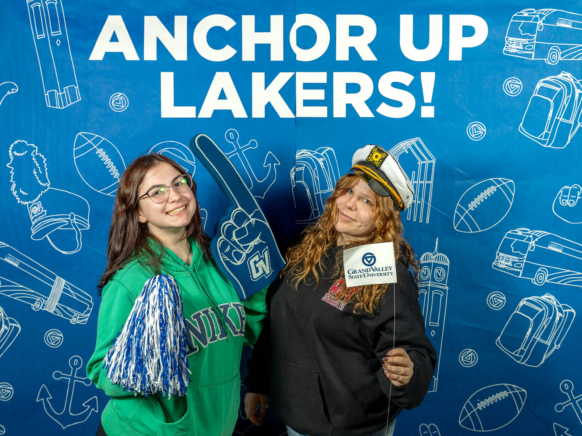two individuals, one on the left holding a blue and white pompom and a foam finger, one on the right holding gvsu flag
